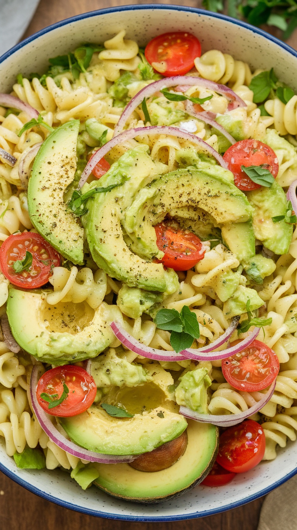 Creamy avocado pasta salad with cherry tomatoes, red onion, and fresh herbs.