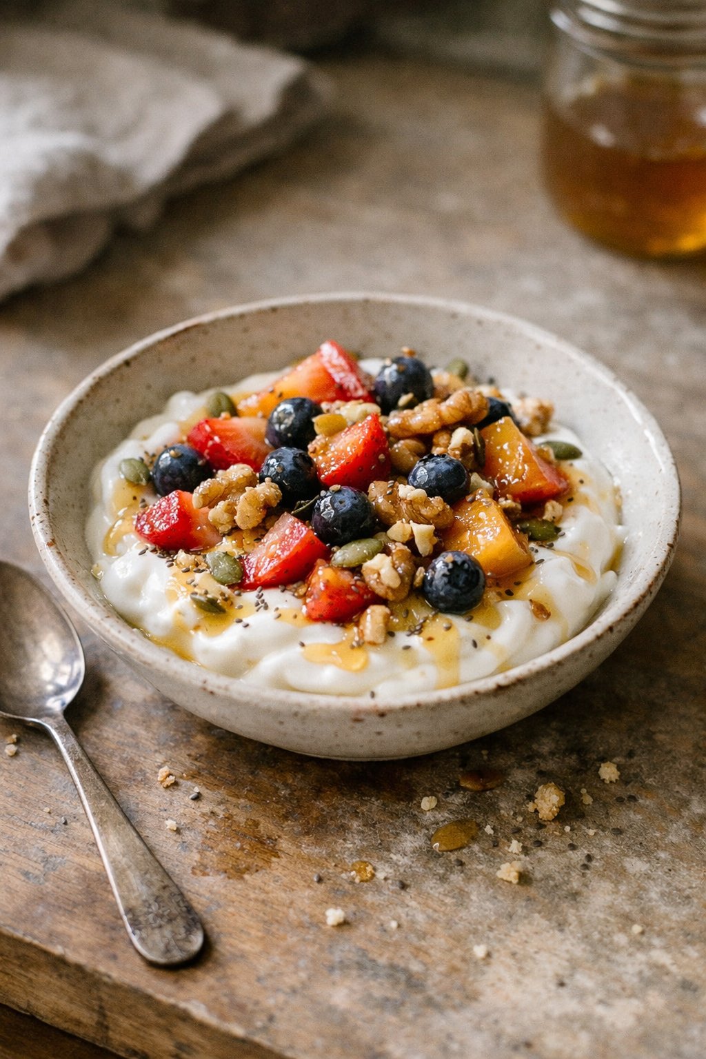A Greek yogurt protein bowl topped with fresh fruit and nuts on a worn kitchen surface, softly lit by natural window light from the side.